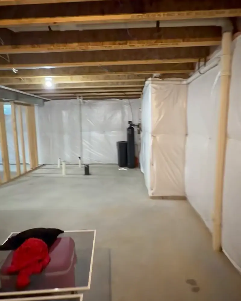 Unfinished basement with framed walls and plastic over the foundation walls